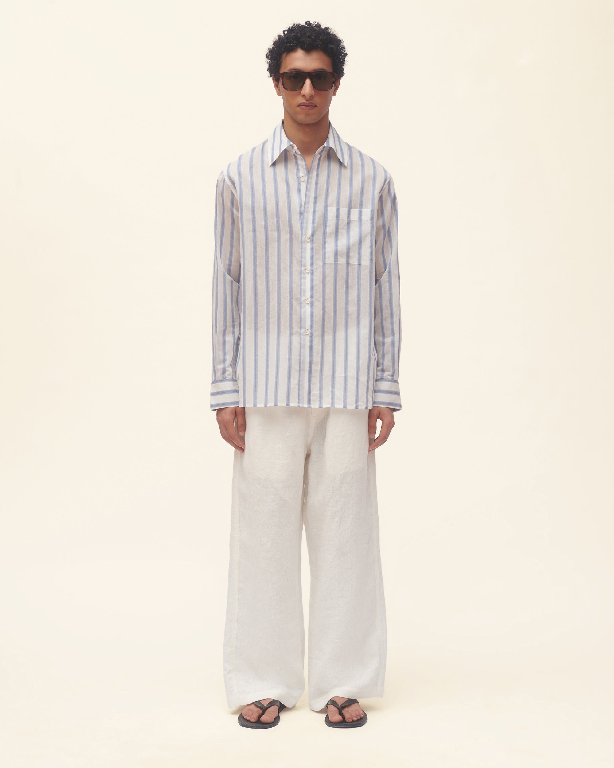 Man wearing a striped shirt and white pants on a beige background