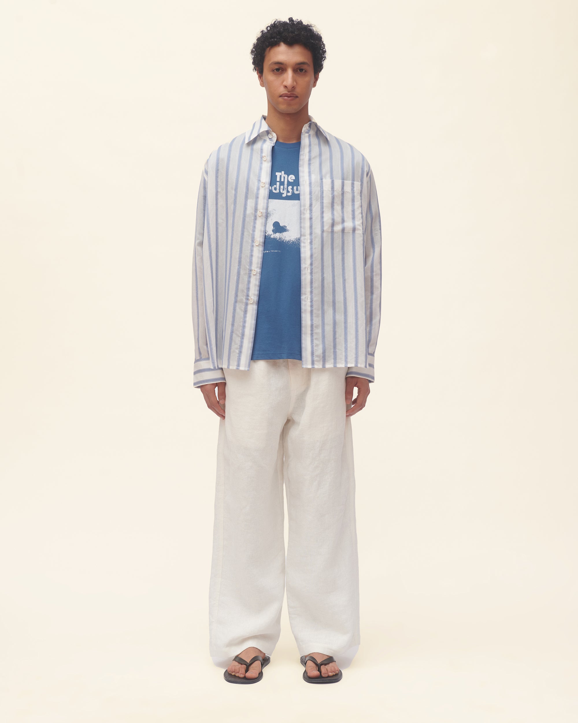 Person wearing a striped shirt and white pants on a beige background