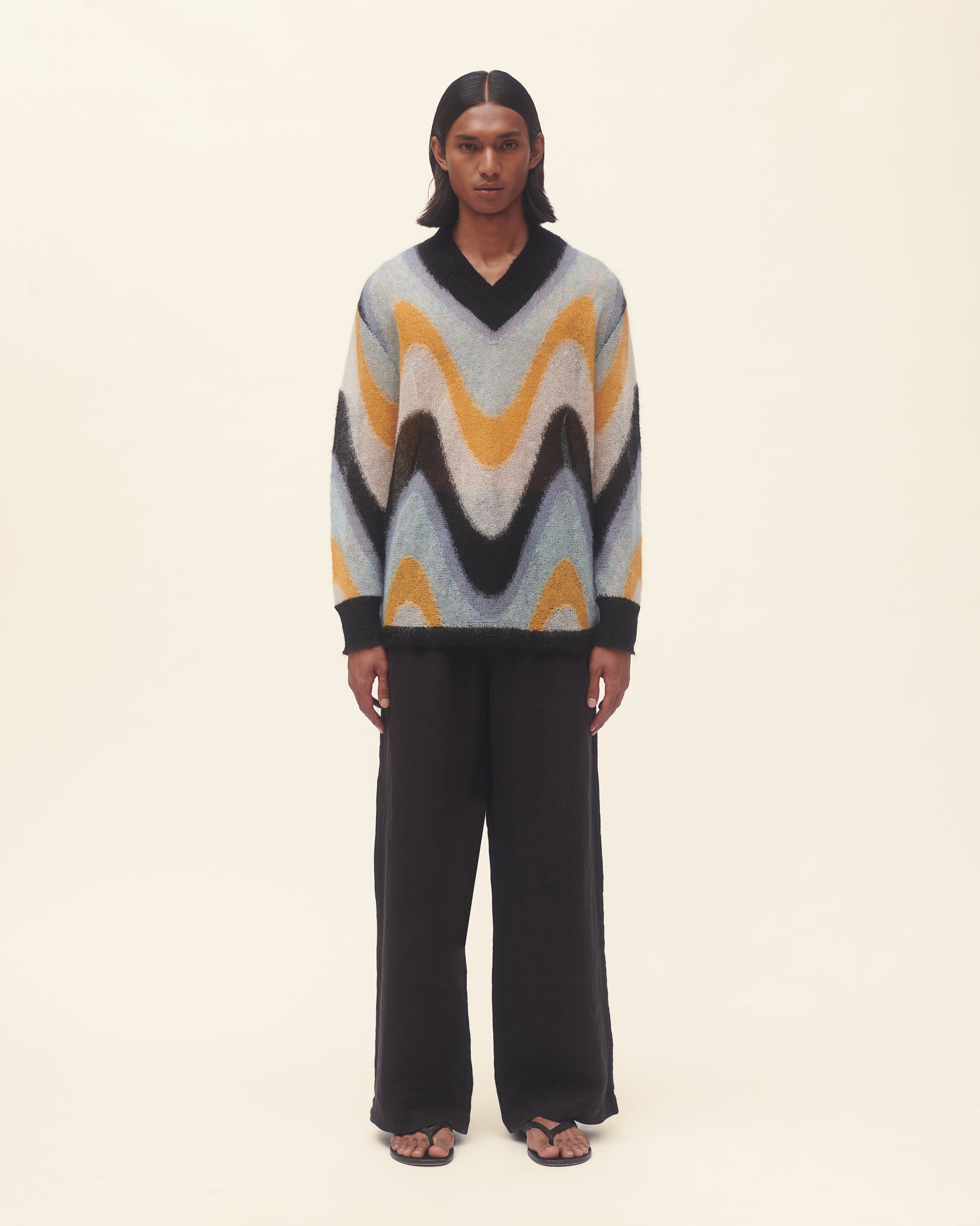 Person wearing a colorful sweater with wavy pattern on a beige background