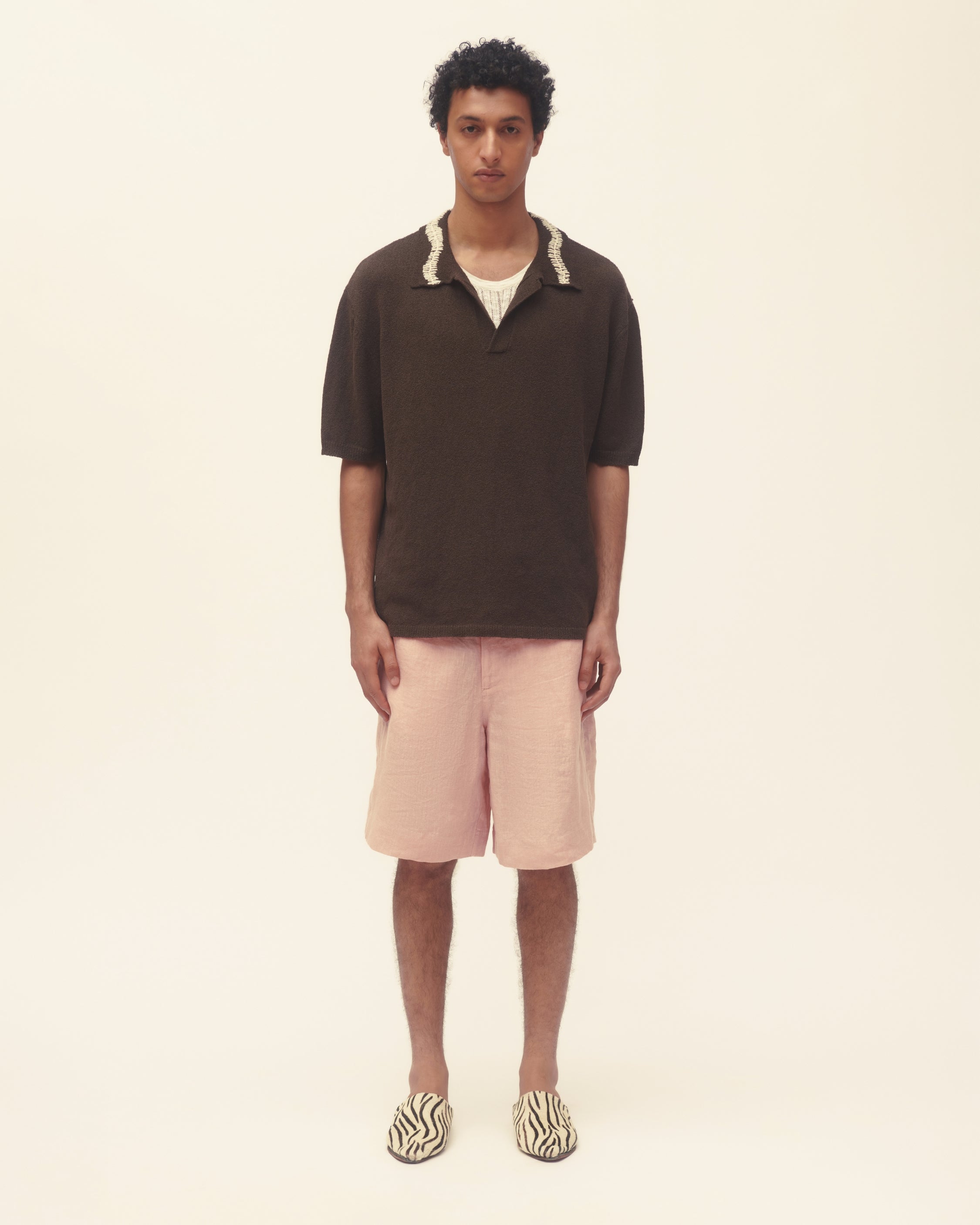 Man wearing a brown polo shirt and light pink shorts on a beige background