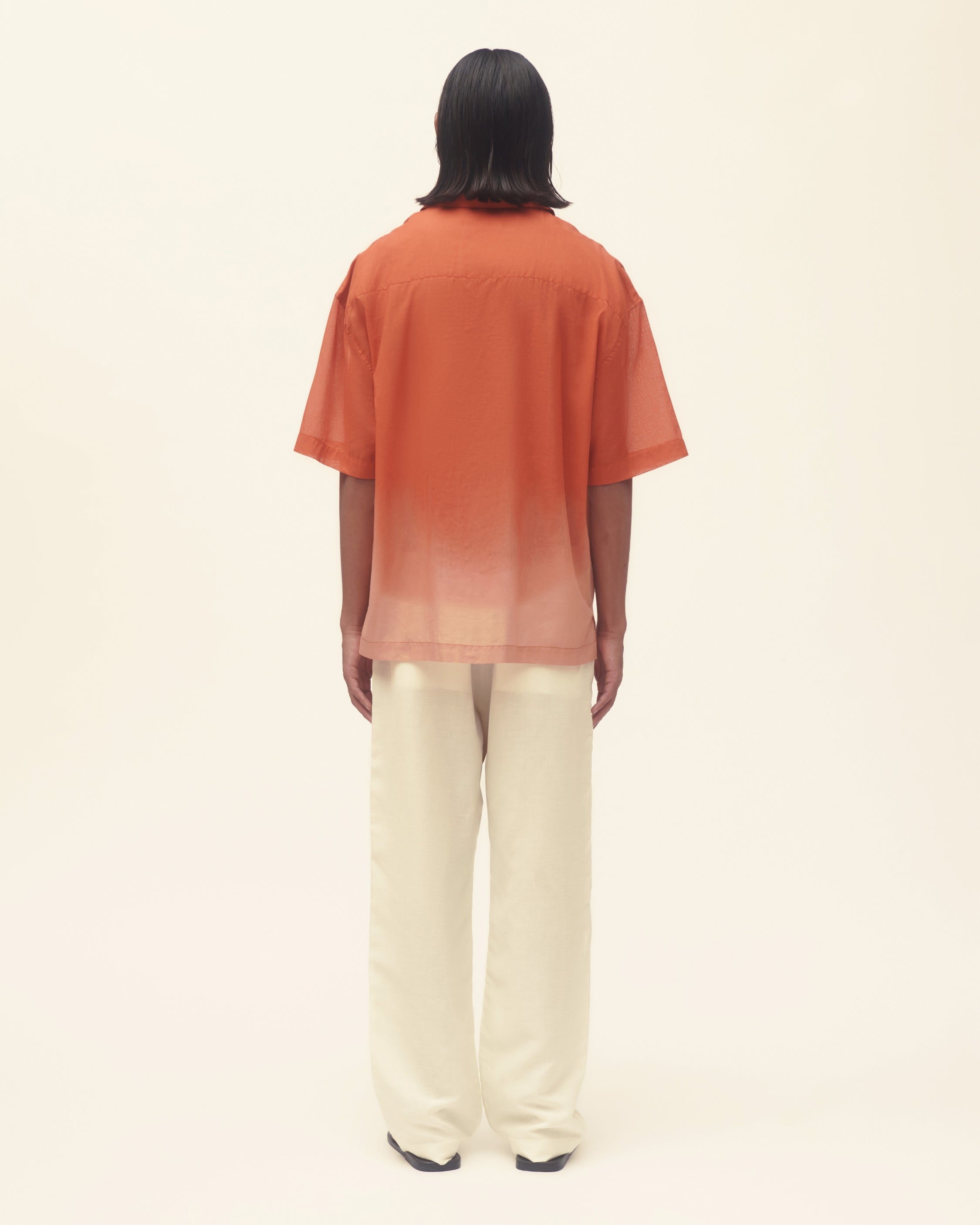 Person wearing an orange to pink gradient shirt and white pants on a beige background