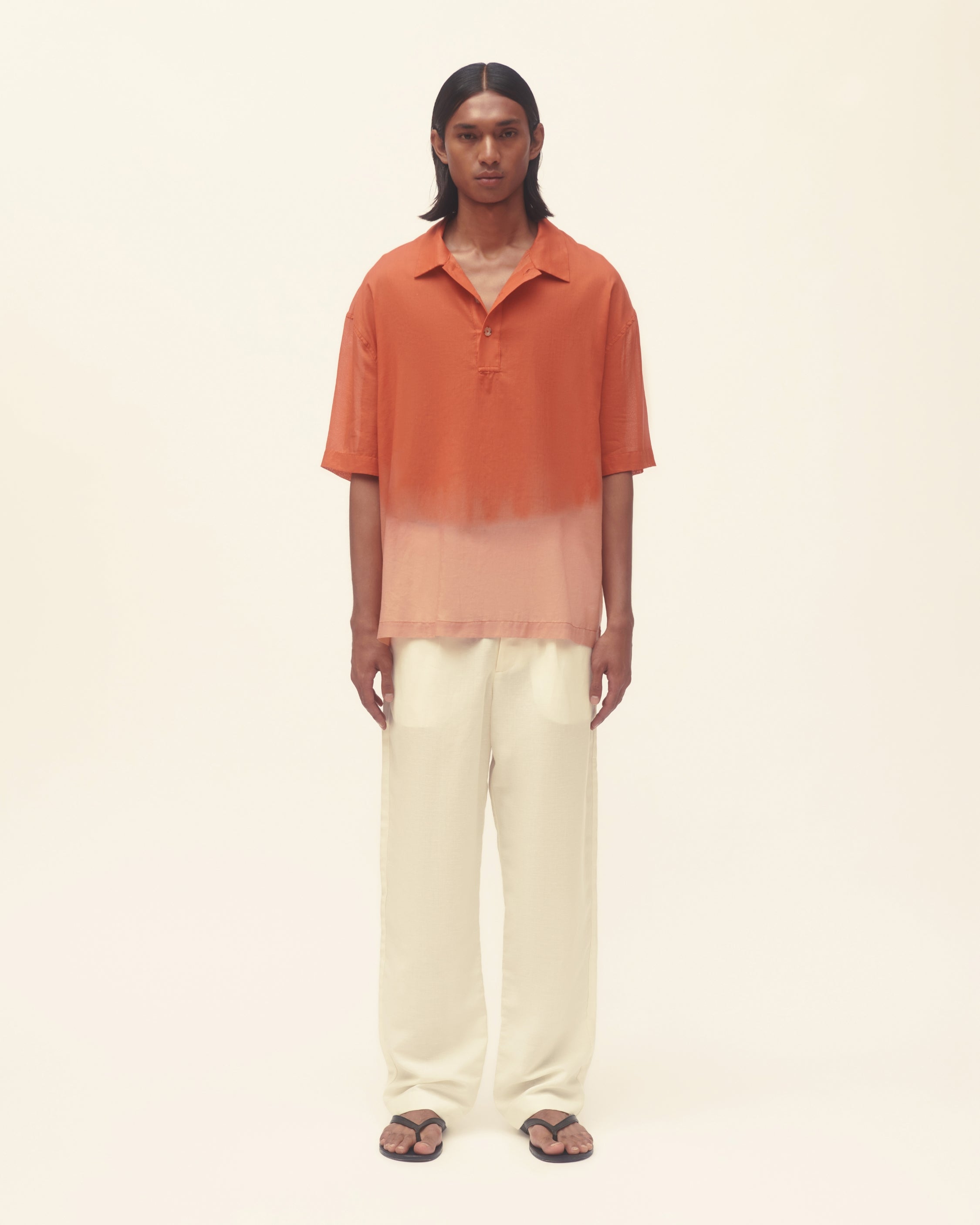 Person wearing an orange to pink gradient shirt and white pants on a beige background