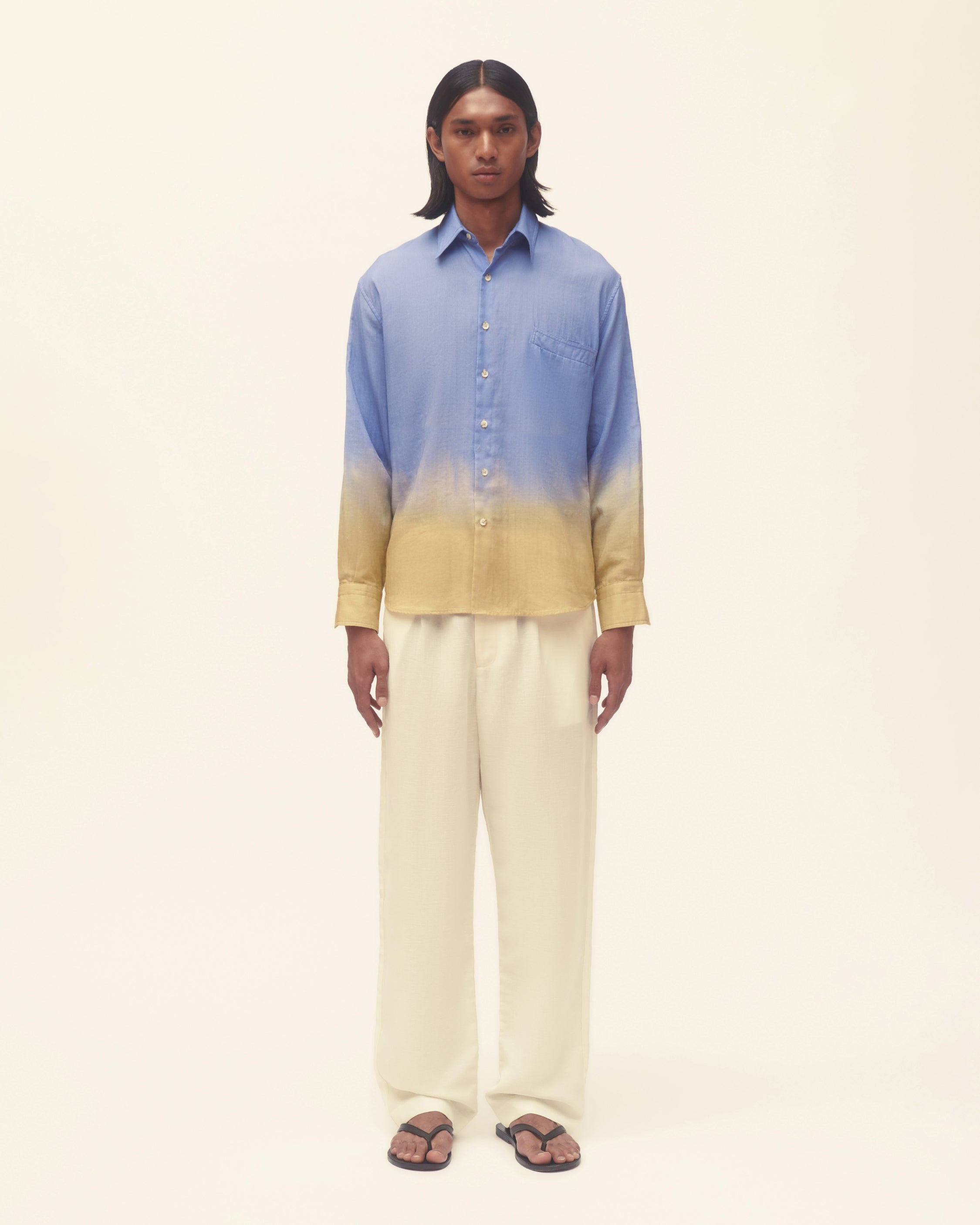 Person wearing a blue and yellow gradient shirt with beige pants on a white background