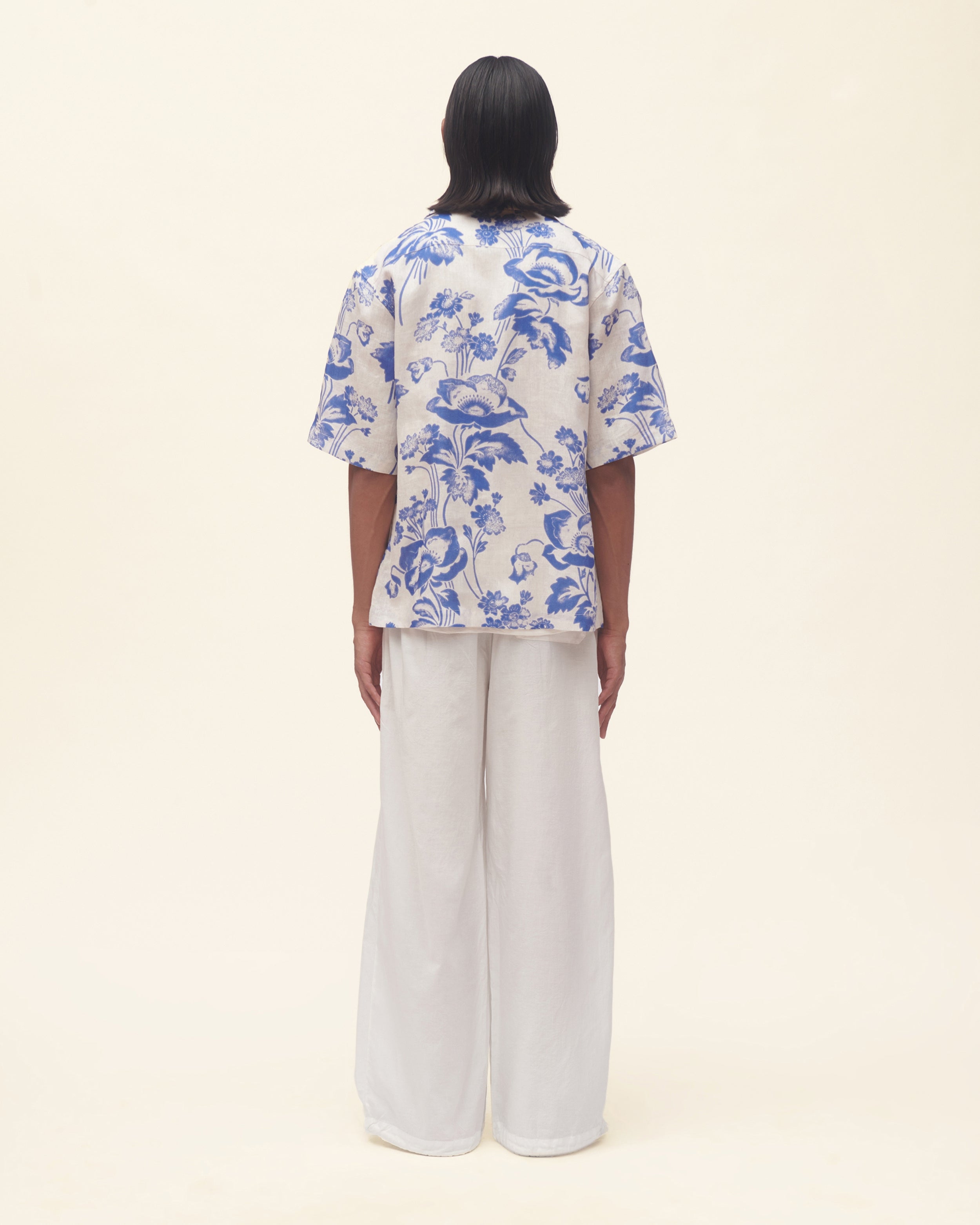 Person wearing a blue floral shirt and white pants on a beige background