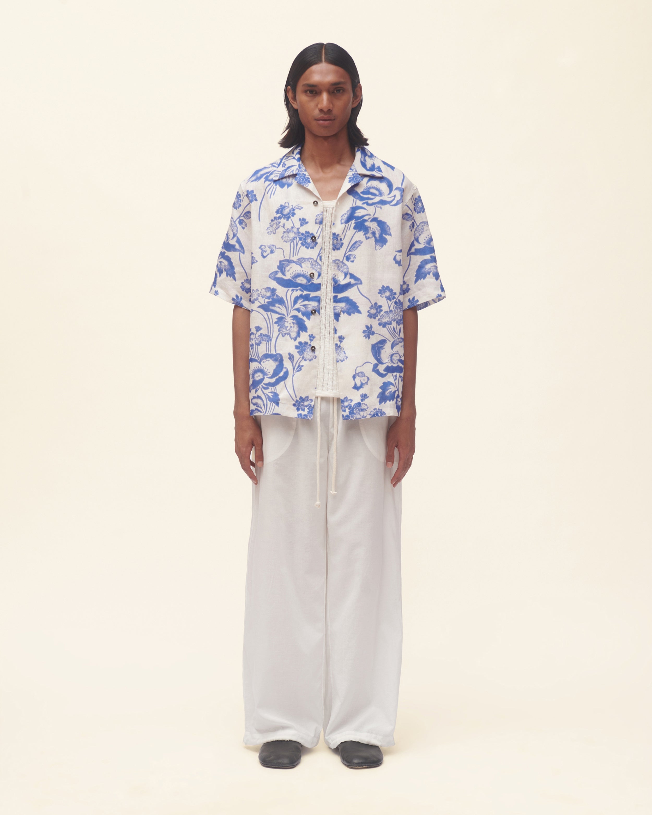 Person wearing a blue floral shirt and white pants on a beige background