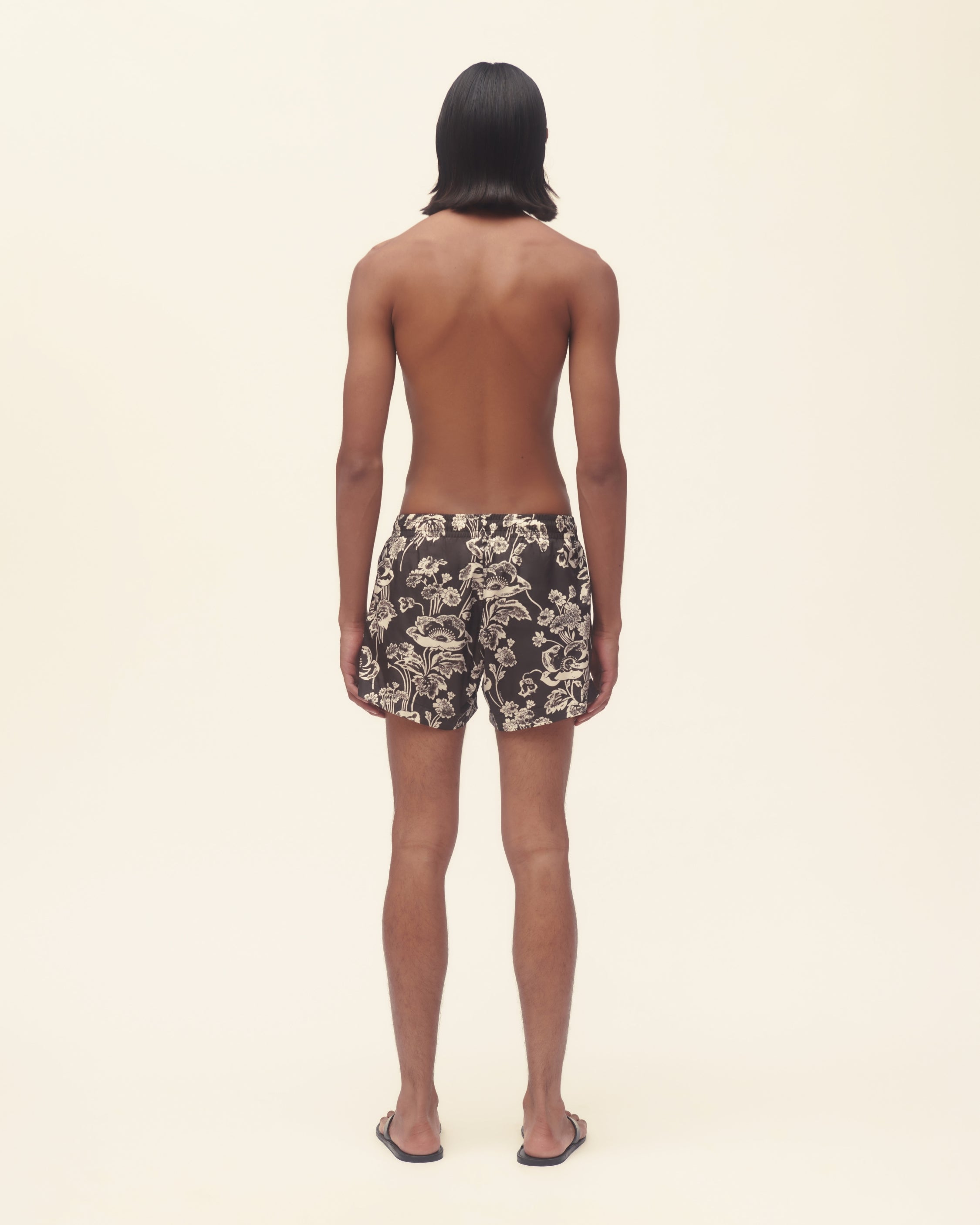 Person wearing floral swim shorts on a beige background