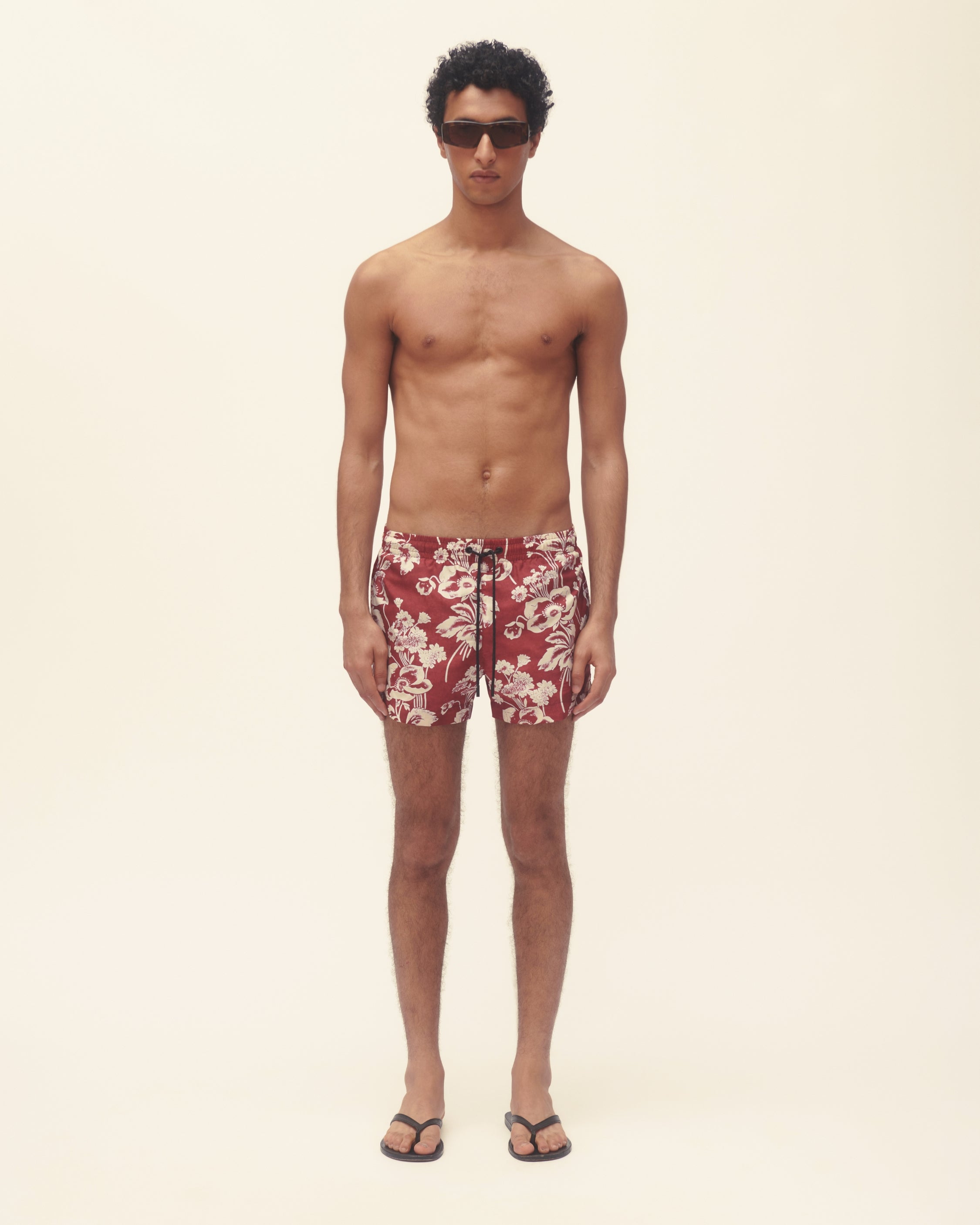 Man wearing red floral swim shorts on a beige background