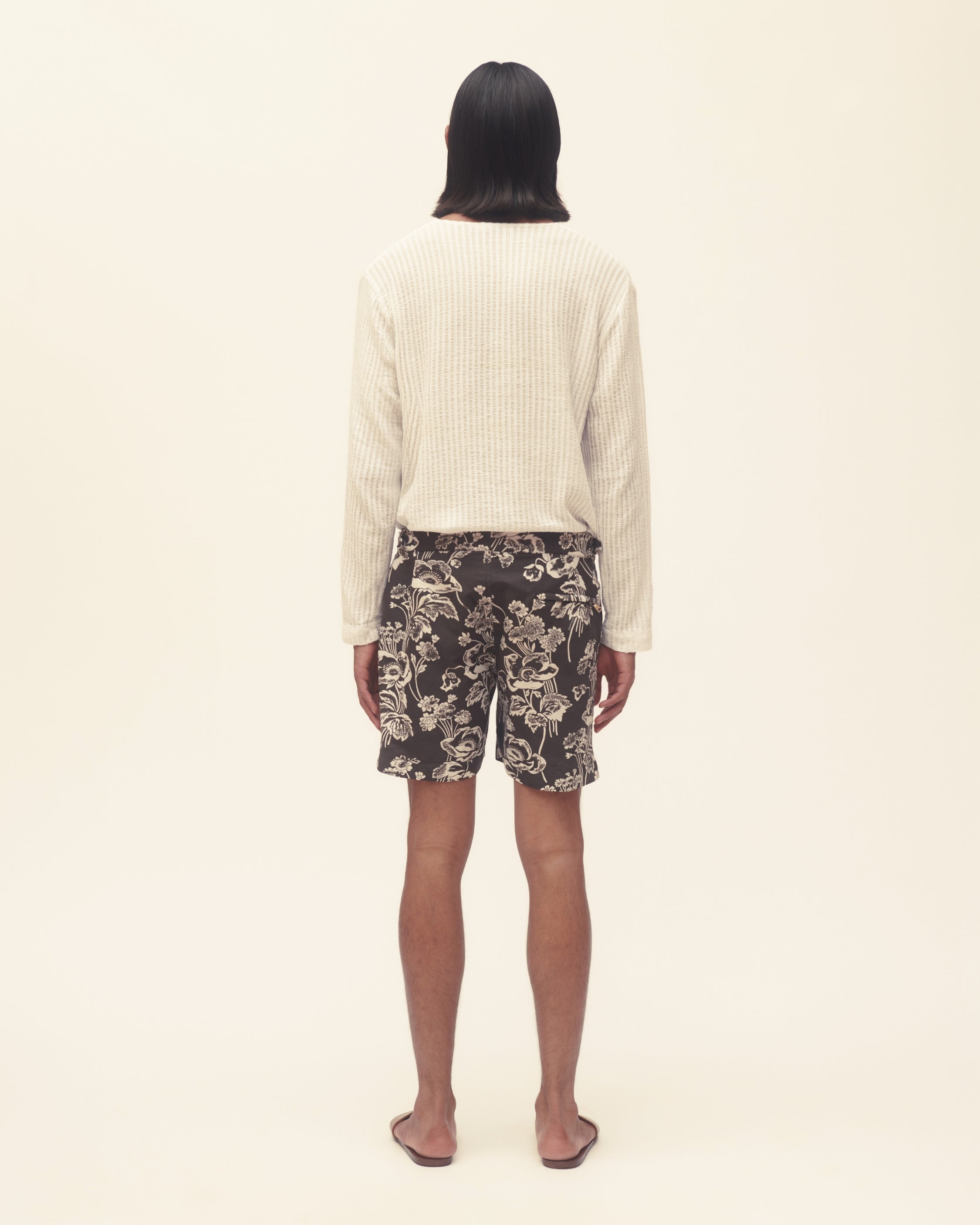 Person wearing a cream sweater and floral shorts on a beige background