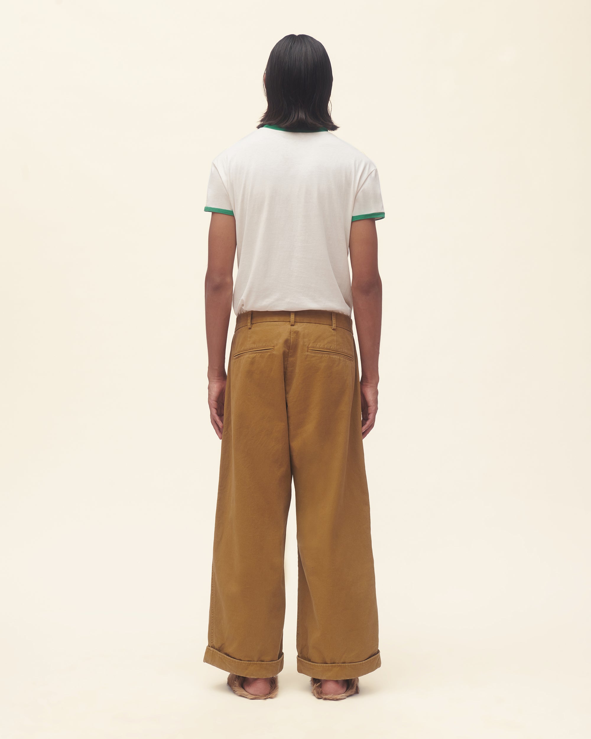Person wearing a white t-shirt with green text and brown pants on a beige background