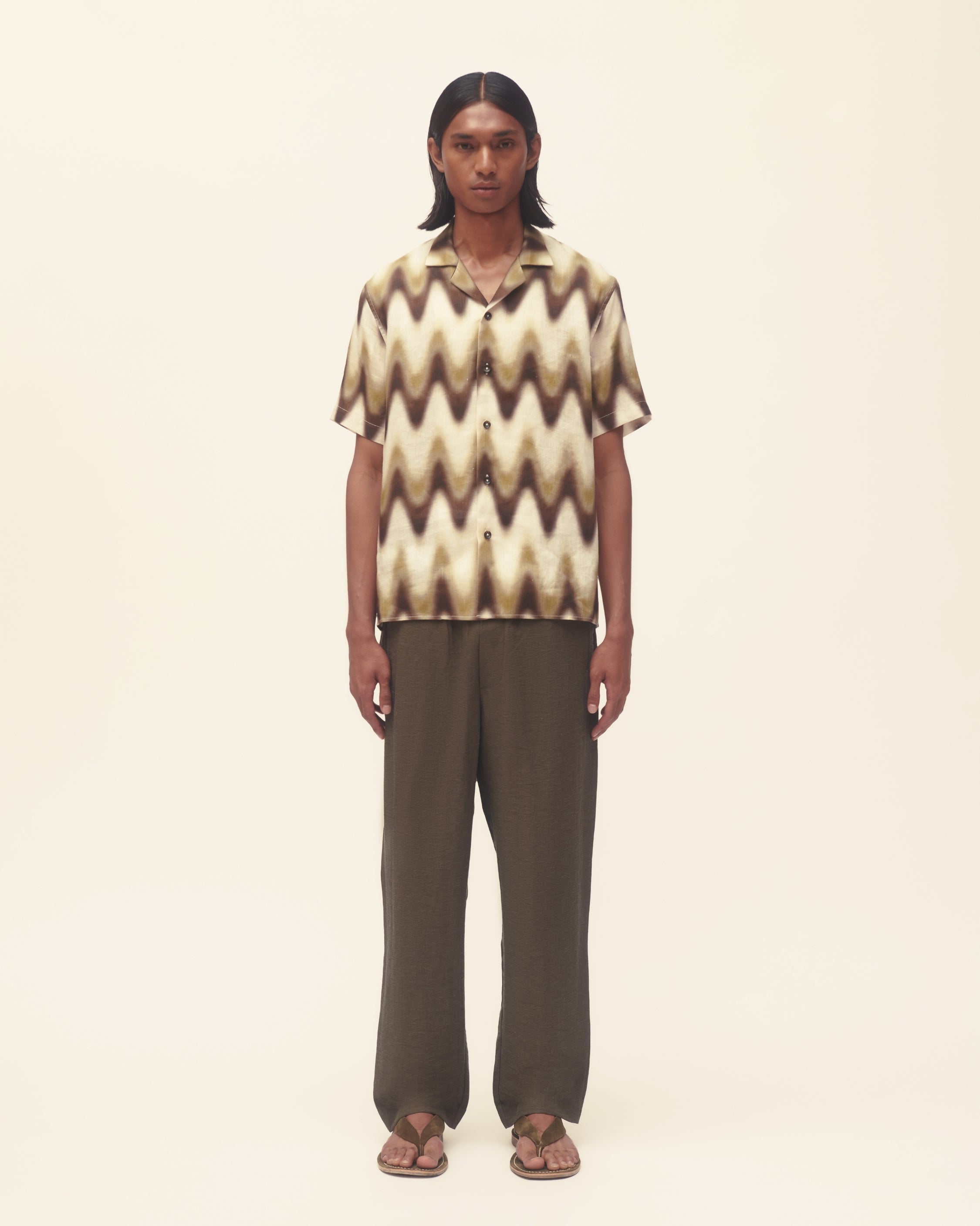 Person wearing a patterned shirt and dark pants on a plain background