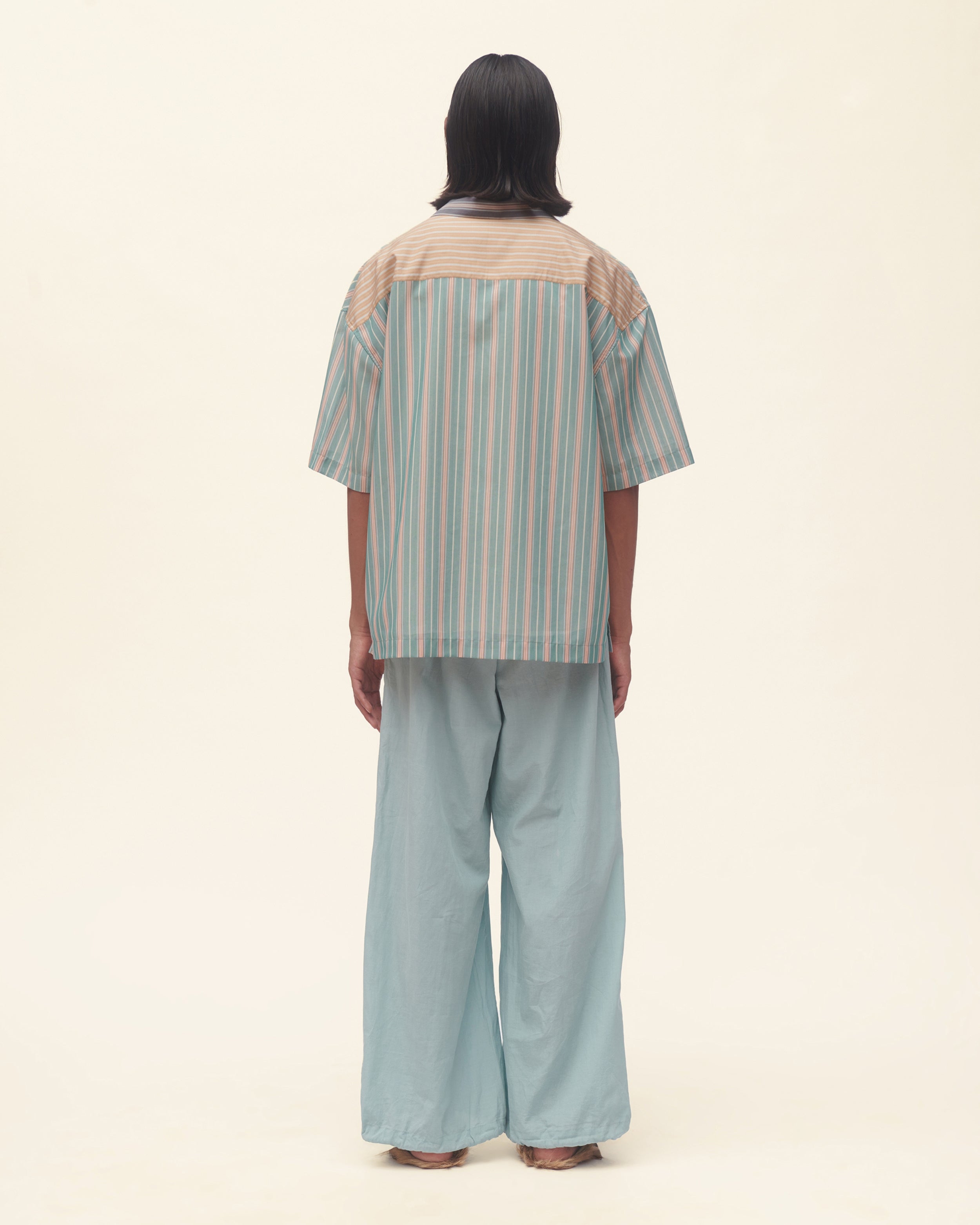 Person wearing a striped shirt and light blue pants on a beige background