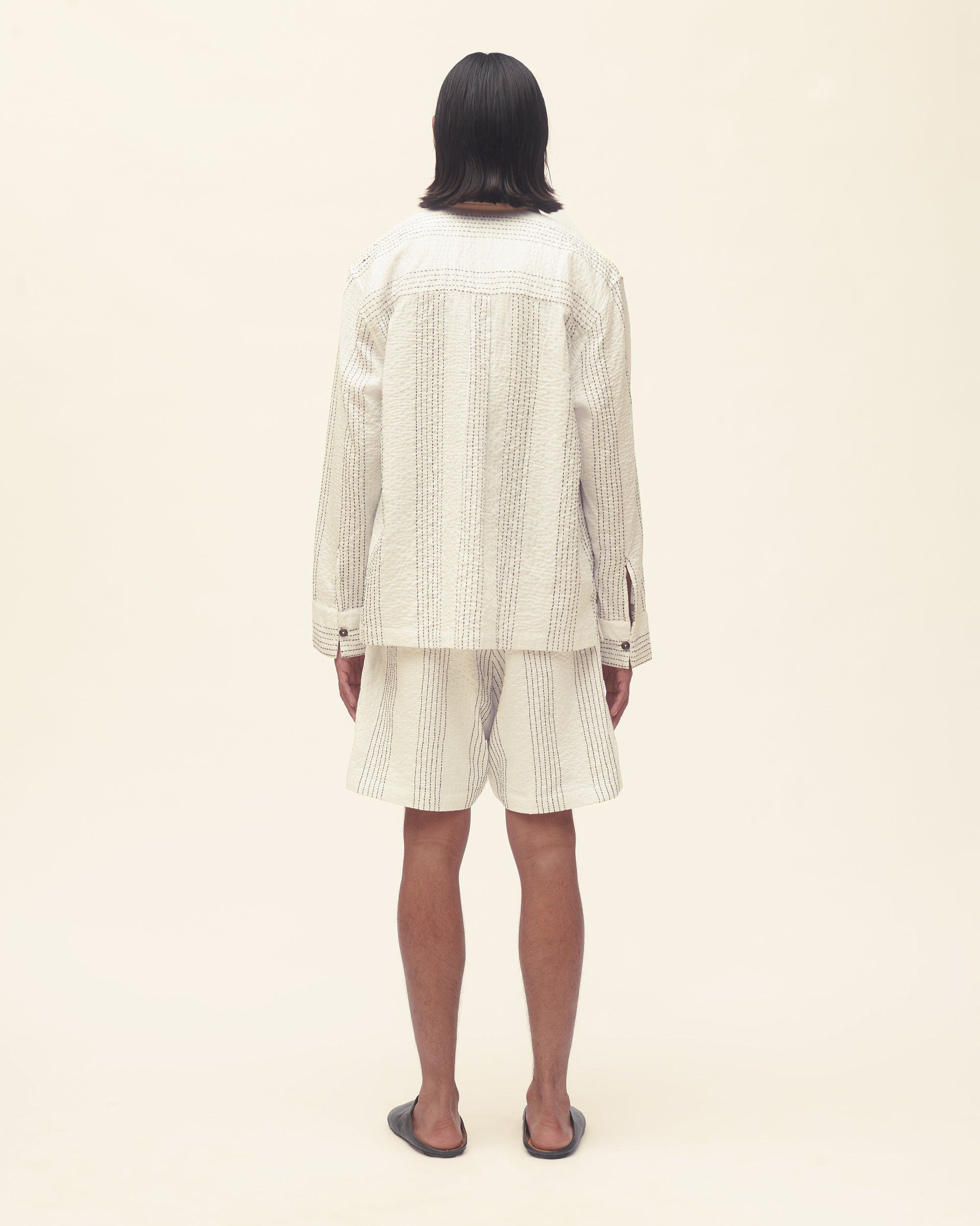 Person wearing a white outfit set with black stripe on a beige background