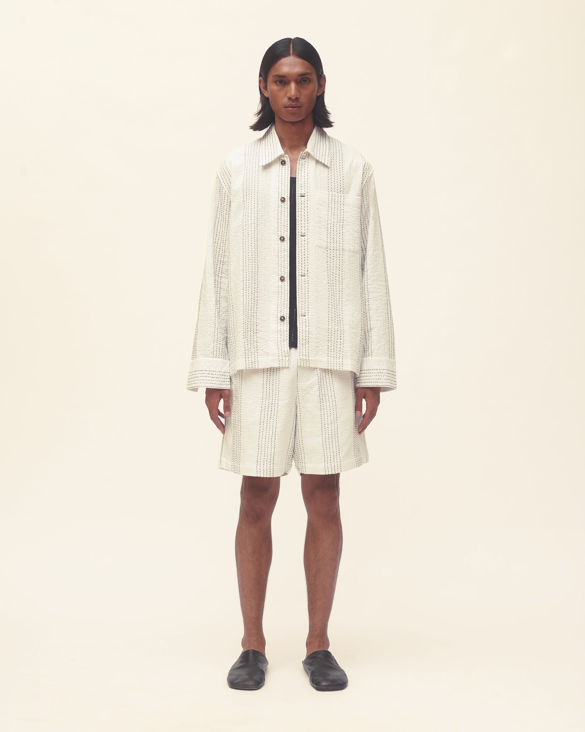 Person wearing a white outfit set with black stripe on a beige background